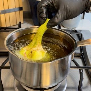 Una persona che indossa guanti neri tiene una banana in una pentola d'acqua