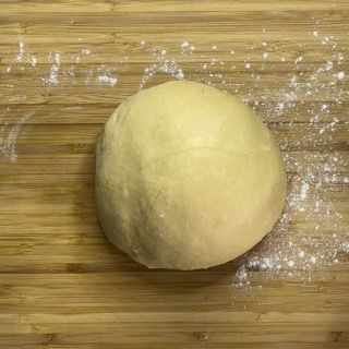 Una palla di pasta è appoggiata su un tagliere di legno.