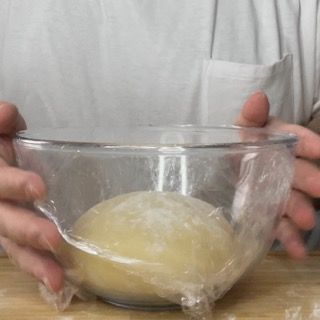 Una persona tiene in mano una ciotola di impasto avvolta nella pellicola trasparente.