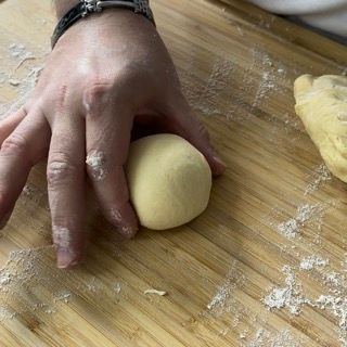 Una persona tiene in mano una palla di pasta su un tagliere di legno.