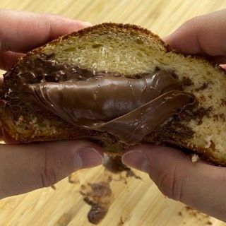 Una persona tiene in mano un pezzo di pane con sopra della crema al cioccolato