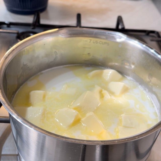 Una pentola di acciaio inossidabile piena di burro e latte sul fornello