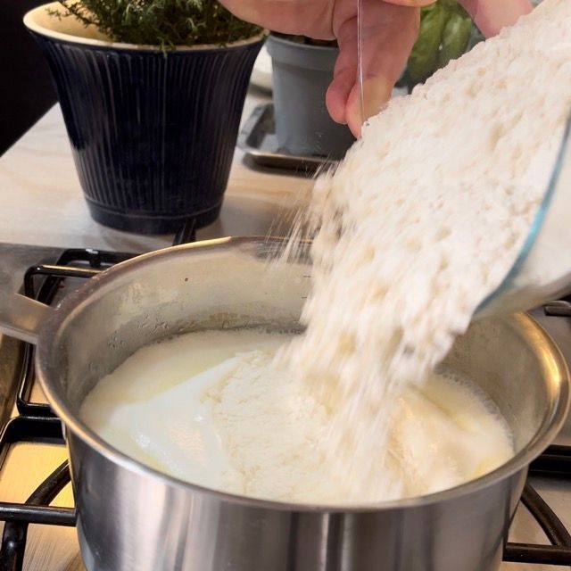 Una persona che versa la farina in una pentola di latte
