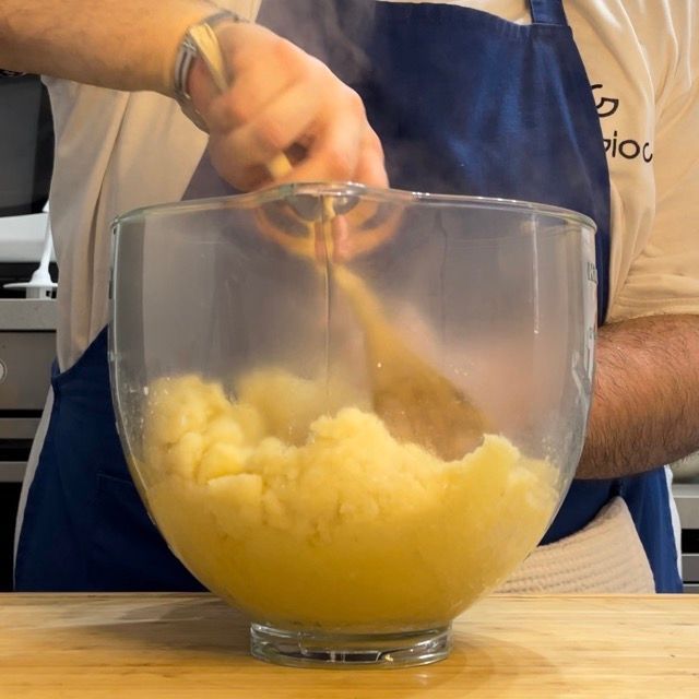 Una persona sta mescolando qualcosa in una ciotola di vetro con un cucchiaio di legno