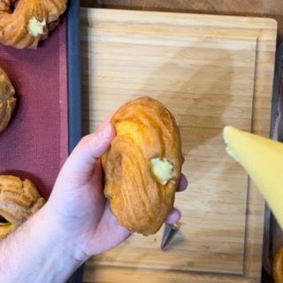 Una persona tiene in mano un dolce davanti a un vassoio di dolci.