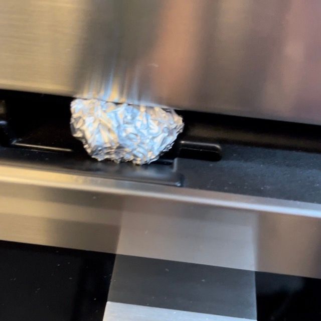 Un pezzo di carta stagnola è appoggiato sulla porta di un forno in acciaio inossidabile.