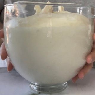 Una persona tiene in mano una ciotola di vetro piena di liquido bianco.