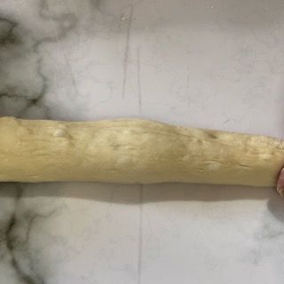 Una persona tiene in mano un pezzo di pasta su una superficie di marmo.