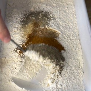 Una persona mescola gli ingredienti in una ciotola di farina con un cucchiaio.