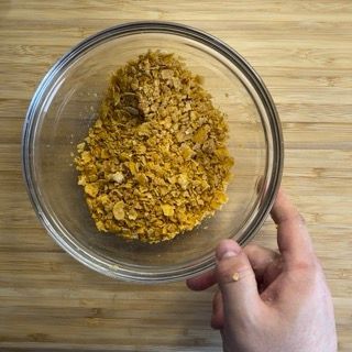 Una persona tiene in mano una ciotola di fiocchi di mais su un tavolo di legno