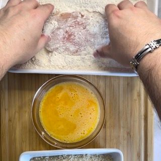 Una persona sta immergendo un pezzo di carne nella farina.