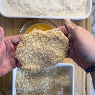 Una persona tiene in mano un pezzo di carne impanata.