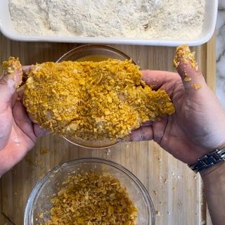 Una persona tiene in mano un pezzo di pollo fritto.