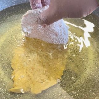 Una persona tiene in mano un pezzo di pollo in una padella.