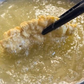 Un pezzo di cibo viene immerso nell'olio con le bacchette.