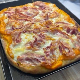 Una pizza con pancetta e formaggio è su una padella