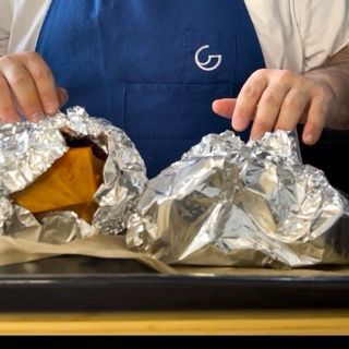 Una persona con un grembiule blu sta avvolgendo il cibo in un foglio di stagnola