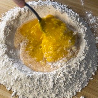 Una persona sta mescolando un liquido giallo in un mucchio di farina.