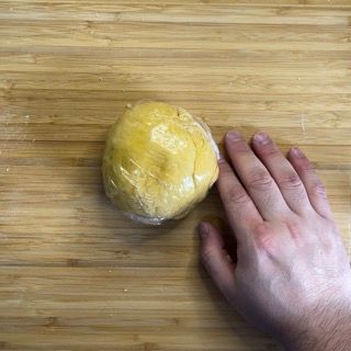 Una persona tiene in mano una palla di pasta su un tagliere di legno.