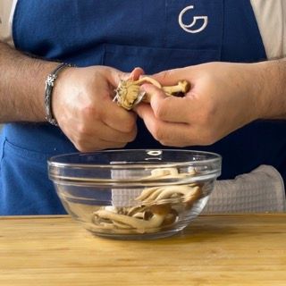 Una persona con un grembiule blu tiene un fungo sopra una ciotola di vetro