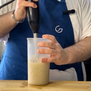 Un uomo con un grembiule blu sta mescolando qualcosa in una tazza