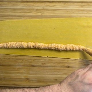 Una persona sta tagliando un pezzo di pasta su un tagliere di legno.