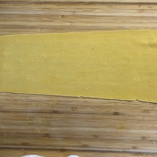 Un pezzo di pasta è appoggiato su un tagliere di legno.