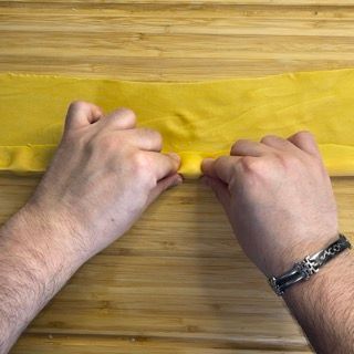 Una persona tiene in mano un pezzo di stoffa gialla su un tavolo di legno.