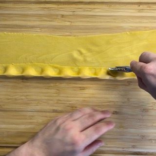 Una persona sta tagliando un pezzo di pasta gialla su un tagliere di legno.