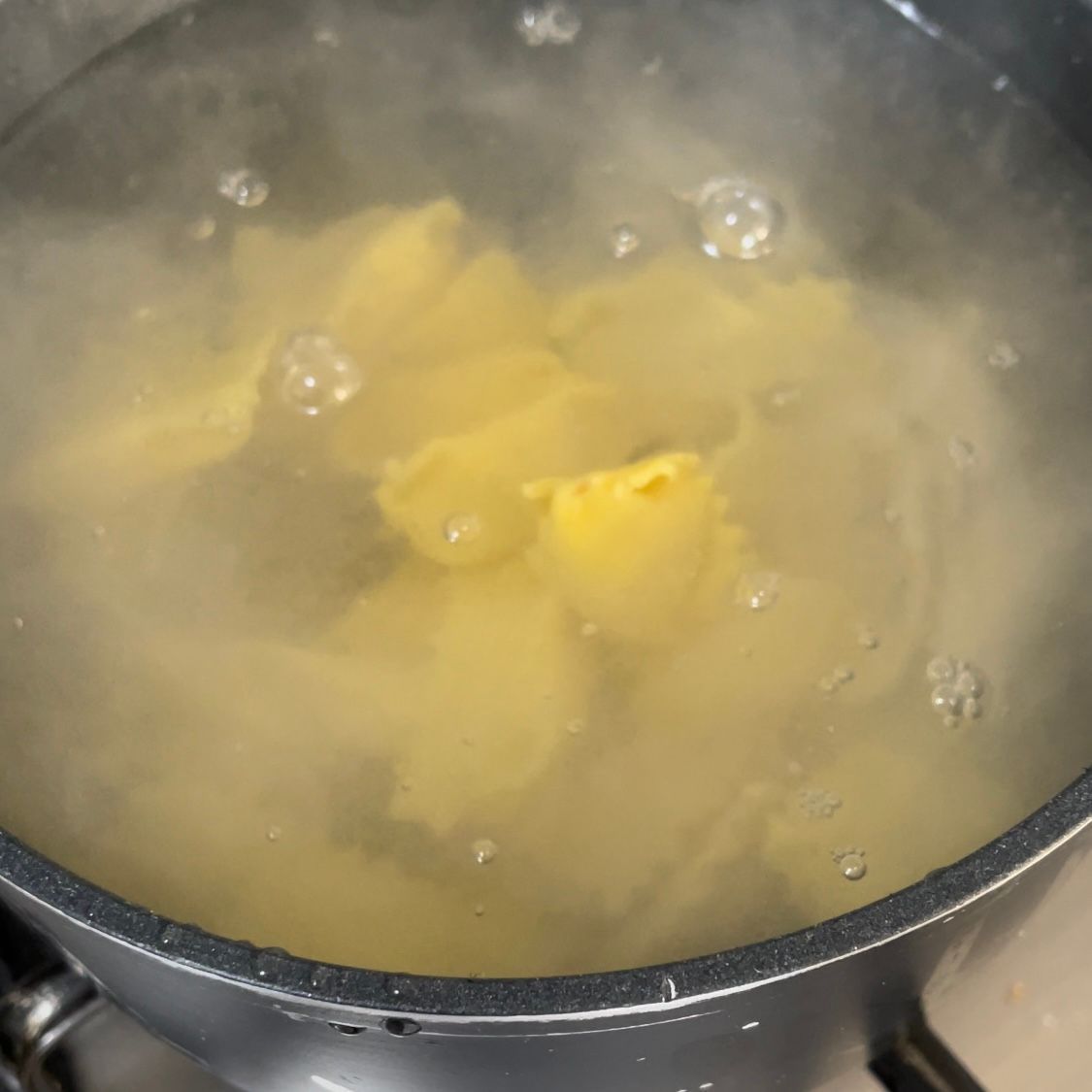 Una pentola con acqua bollente e pasta dentro.