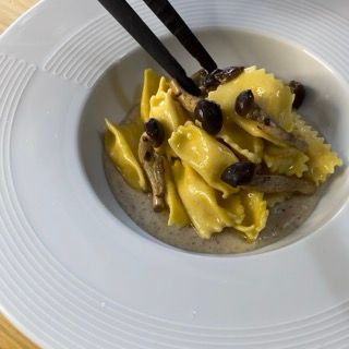 Un piatto bianco con sopra pasta e funghi con le bacchette