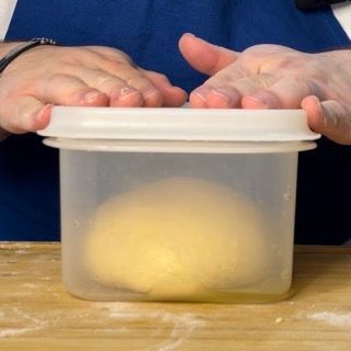 Una persona tiene in mano un contenitore di plastica con una palla di pasta dentro