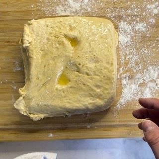 Una persona tiene in mano un pezzo di pasta su un tagliere di legno.