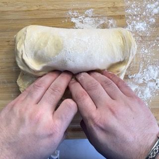 Una persona sta piegando un pezzo di pasta su un tagliere di legno.