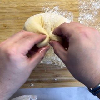 Una persona sta impastando l'impasto su un tagliere di legno.