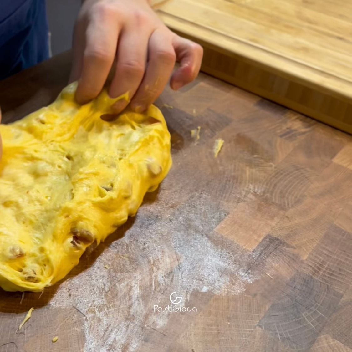Una persona tiene in mano un pezzo di pasta su un tagliere di legno.