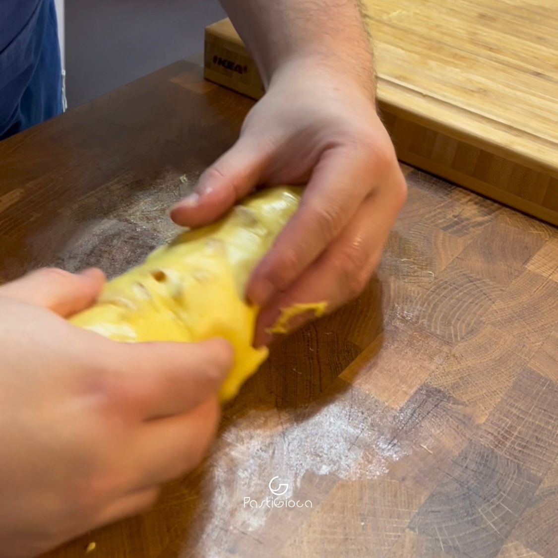 Una persona tiene in mano un pezzo di pasta su un tavolo di legno.