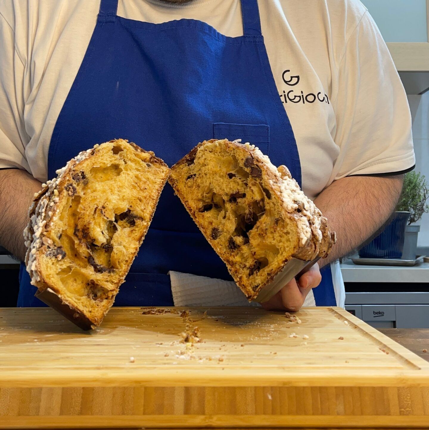 Un uomo con un grembiule blu tiene in mano una pagnotta tagliata a metà