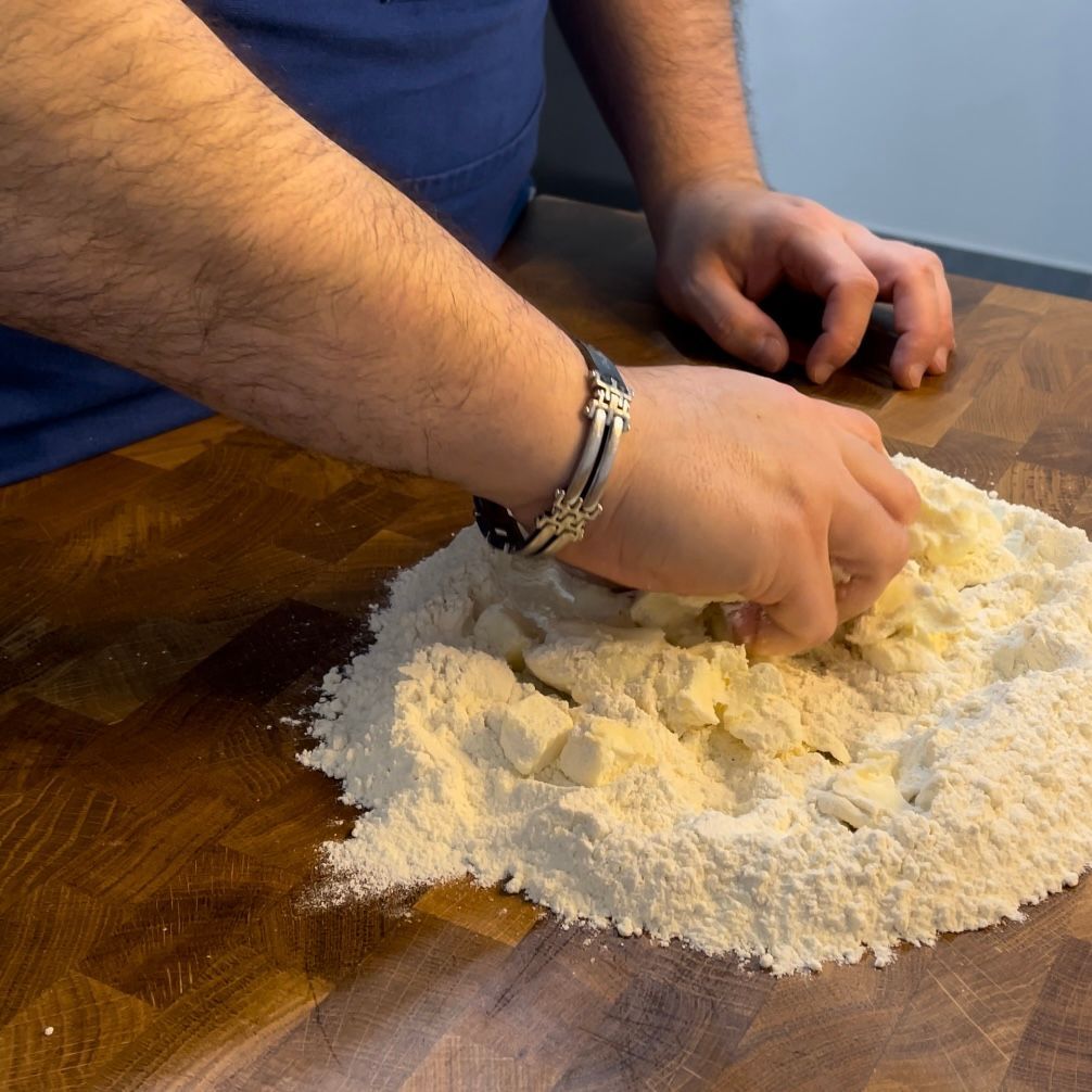 Un uomo che indossa un braccialetto sta impastando la pasta su un tagliere di legno