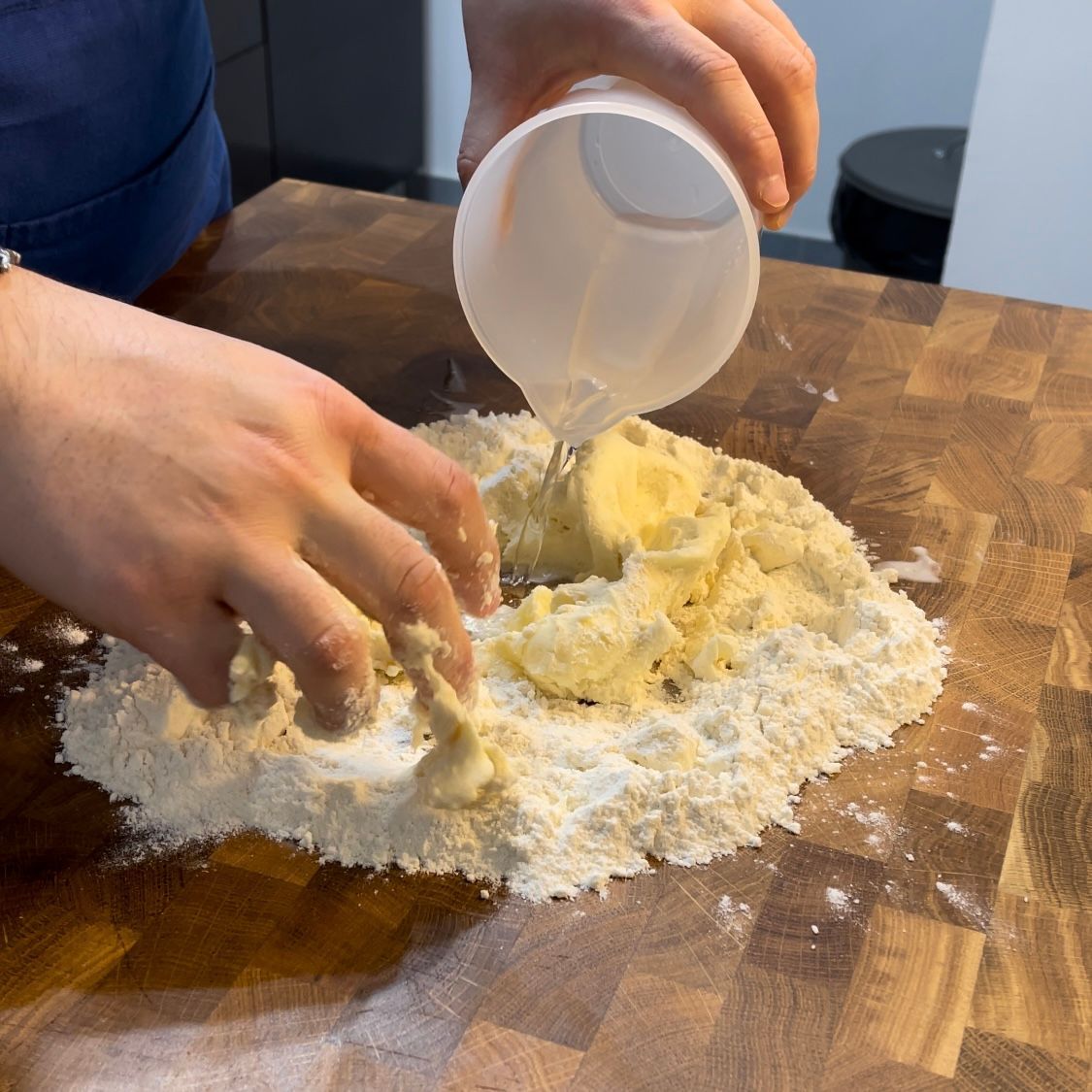 Una persona sta versando del liquido in un mucchio di farina su un tagliere.