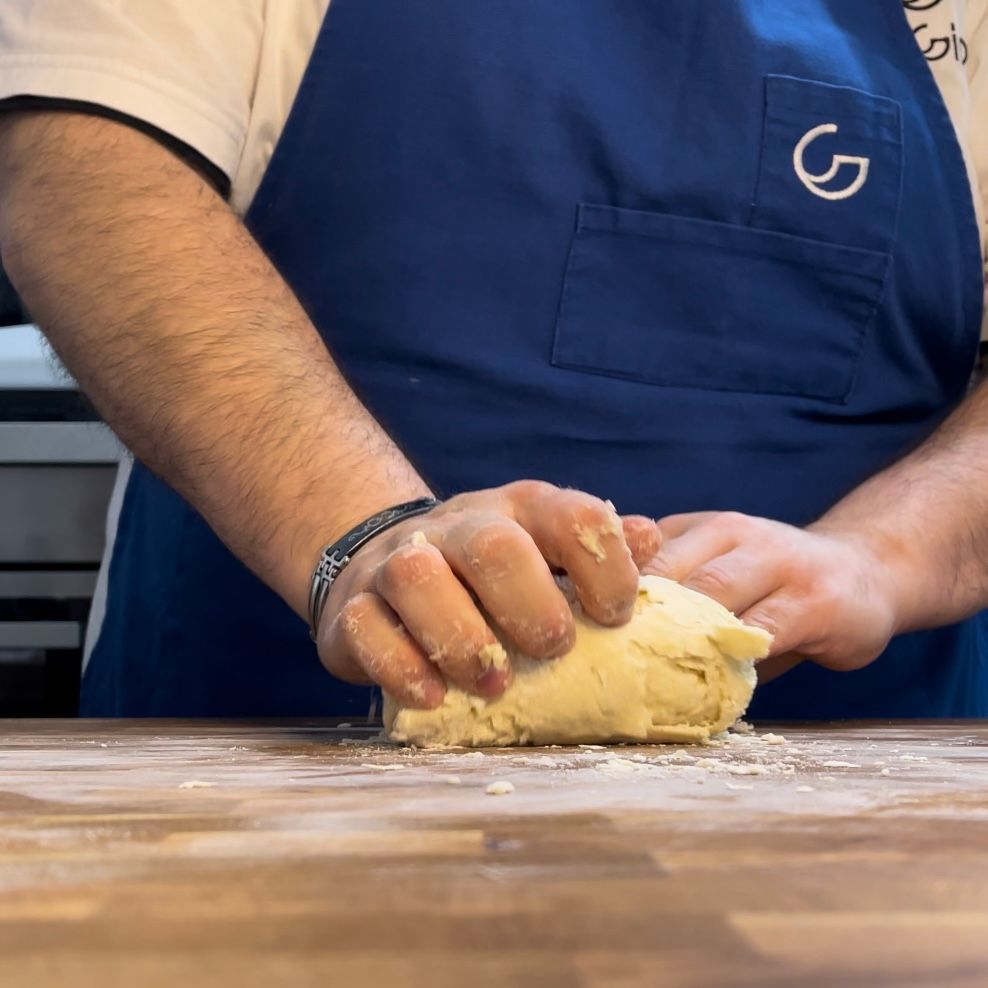 Un uomo con un grembiule blu sta impastando la pasta su un tagliere