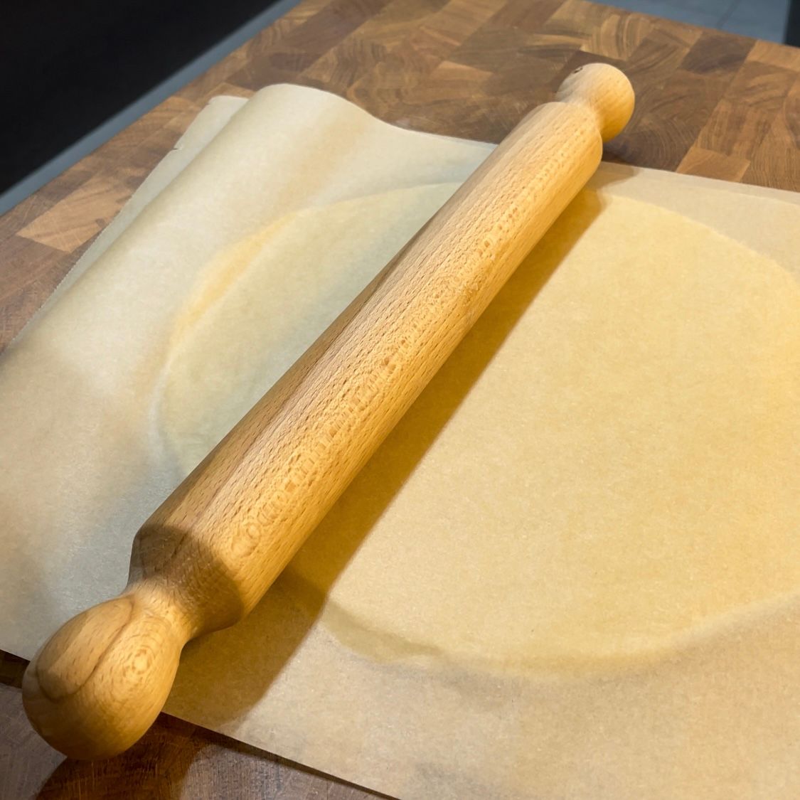 Un mattarello di legno è appoggiato su un pezzo di carta da forno