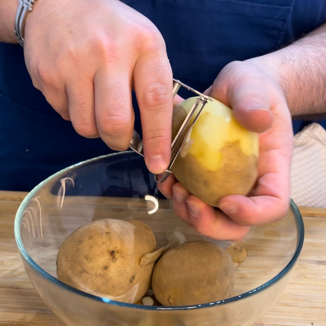 Una persona sta sbucciando le patate in una ciotola di vetro