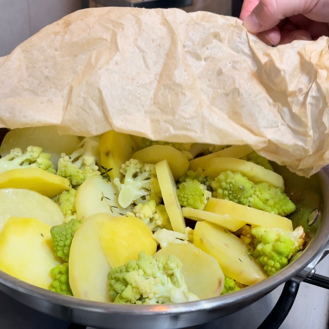 Una persona tiene un pezzo di carta marrone sopra una padella di patate e broccoli