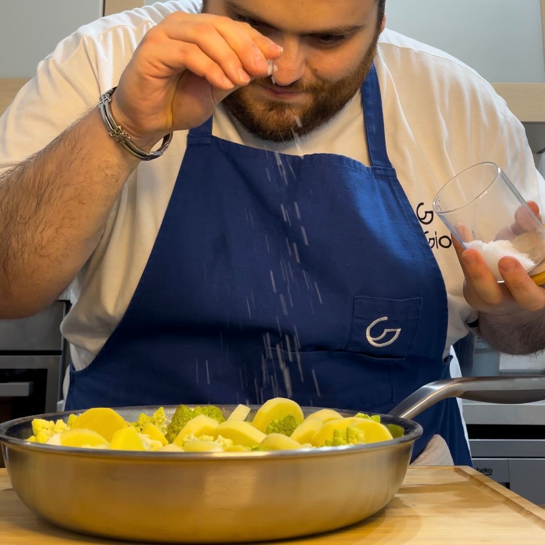 Un uomo con un grembiule sta aggiungendo sale a una padella di cibo