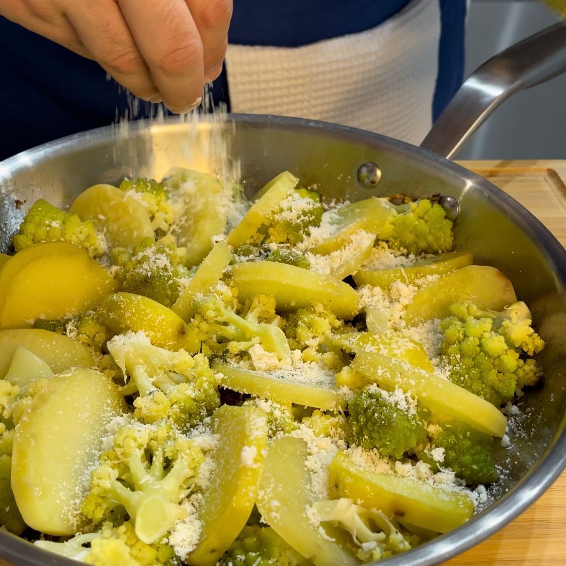 Una persona sta cospargendo il formaggio su una padella di verdure