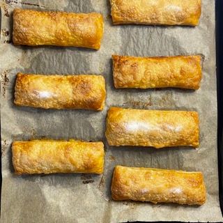 Un mucchio di rotoli di pasta sfoglia sono appoggiati su un pezzo di carta marrone.