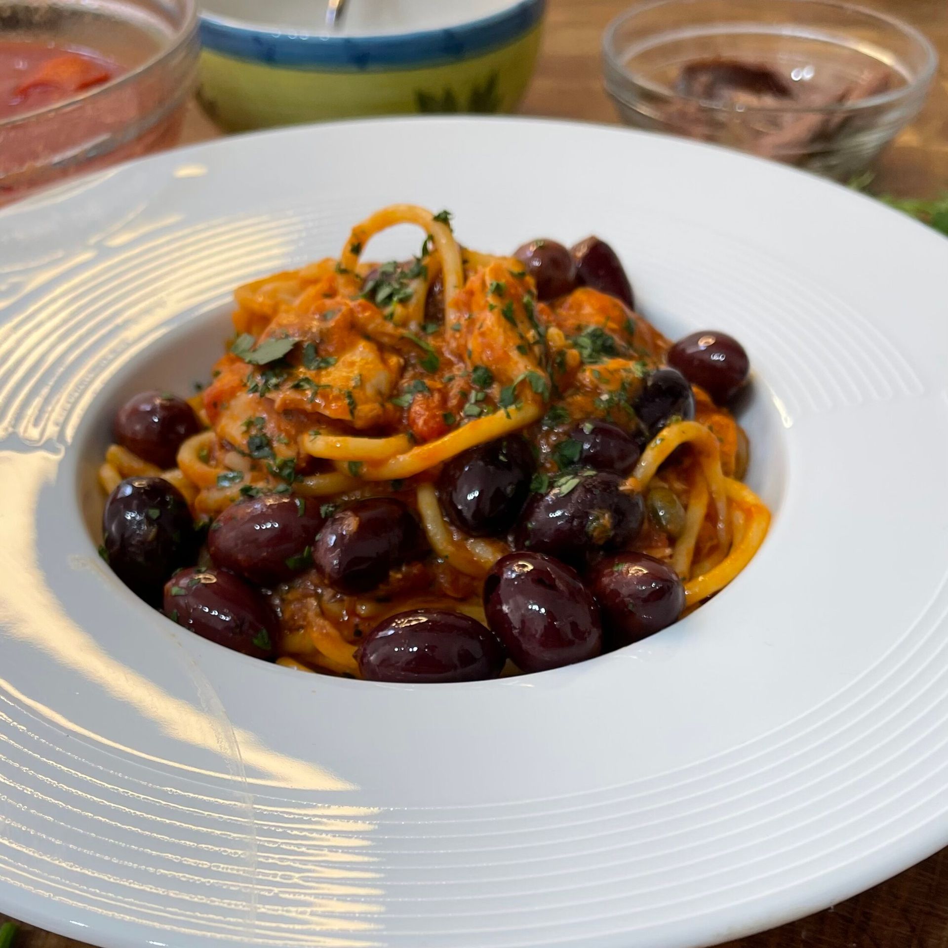 Un piatto bianco con sopra spaghetti e olive su un tavolo