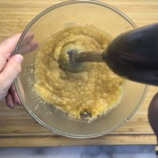 Una persona tiene in mano un frullatore sopra una ciotola di cibo.