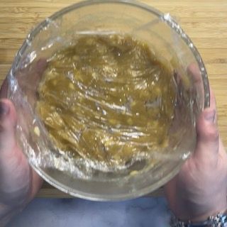 Una persona tiene in mano una ciotola di vetro ricoperta di pellicola trasparente.